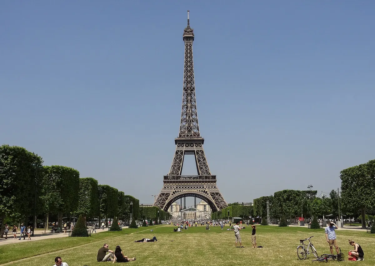 The Eiffel Tower seen from the lawn of the Champ de Mars on a clear day, with people sitting on the grass