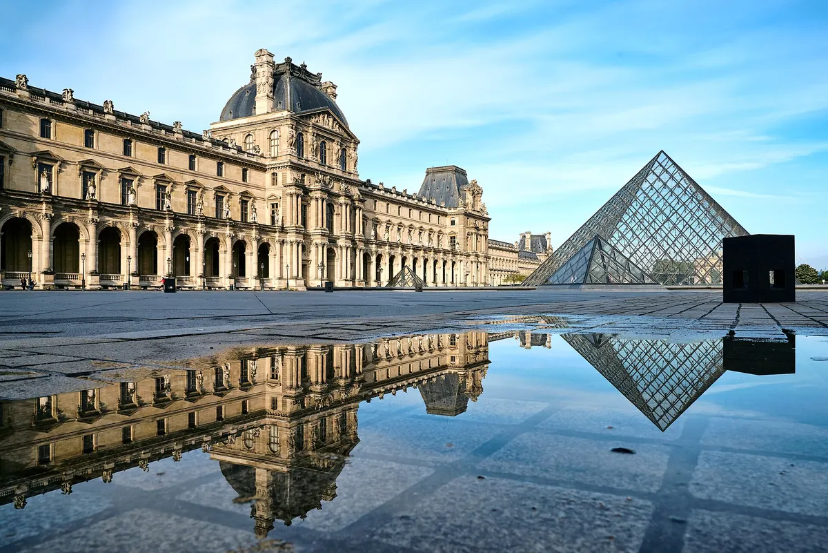 The glass Pyramid and the north facade of the Louvre's Denon wing reflected in a puddle, clear sky
