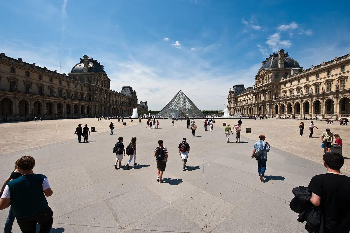 Visitors walking across the Cour Napoléon toward the glass Pyramid of the Louvre, daytime