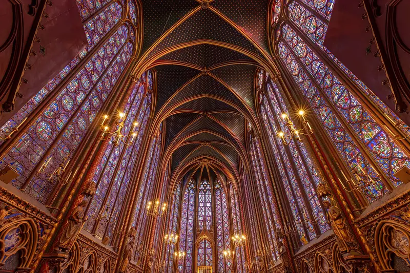 The upper chapel of the Sainte-Chapelle seen from the nave: tall stained glass bays rise on both sides to a dark star-patterned vault