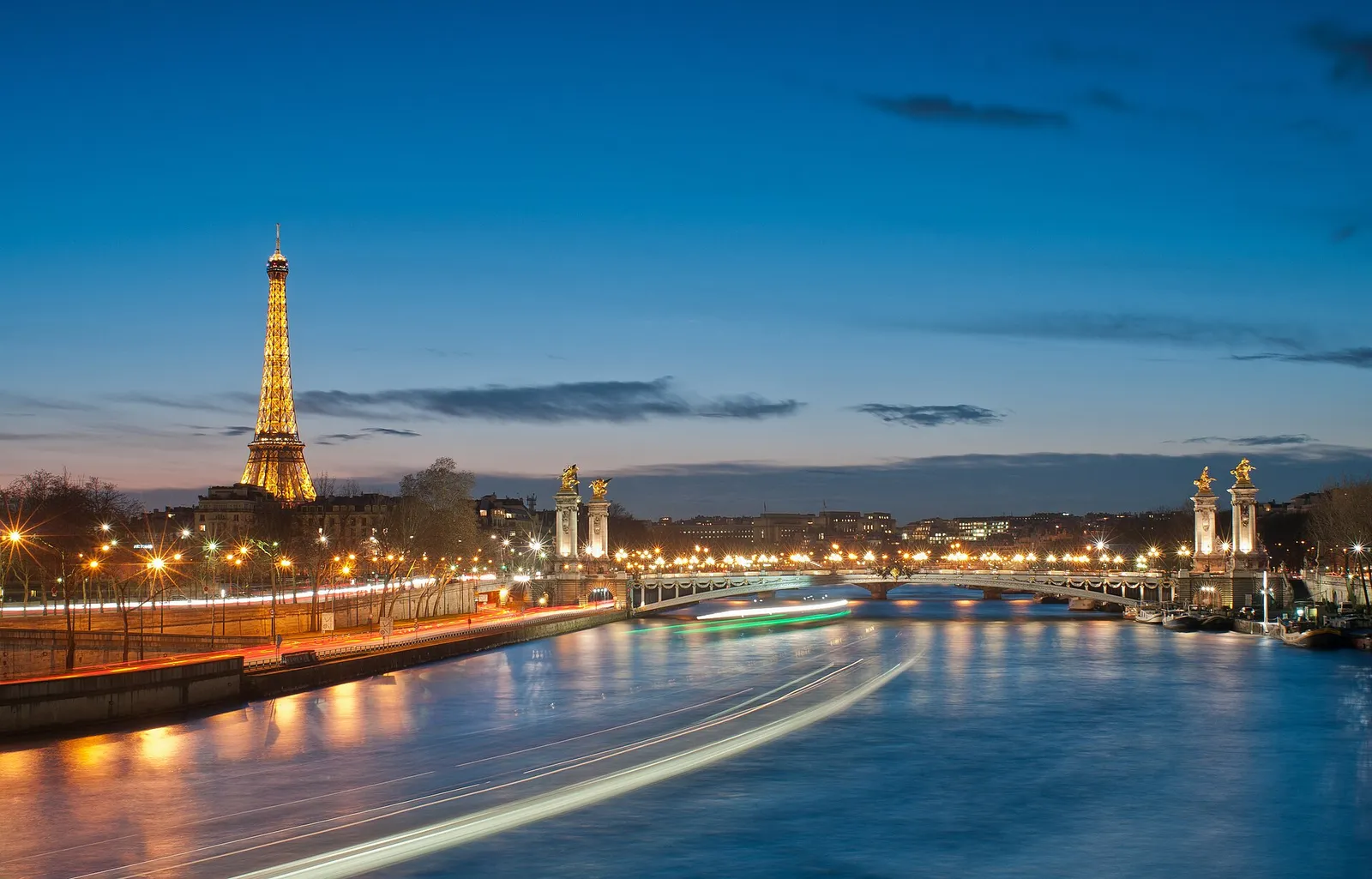 Lit Eiffel Tower and Pont Alexandre III with light trails of a passing boat on the river, Seine between the Invalides and the Alma, dusk