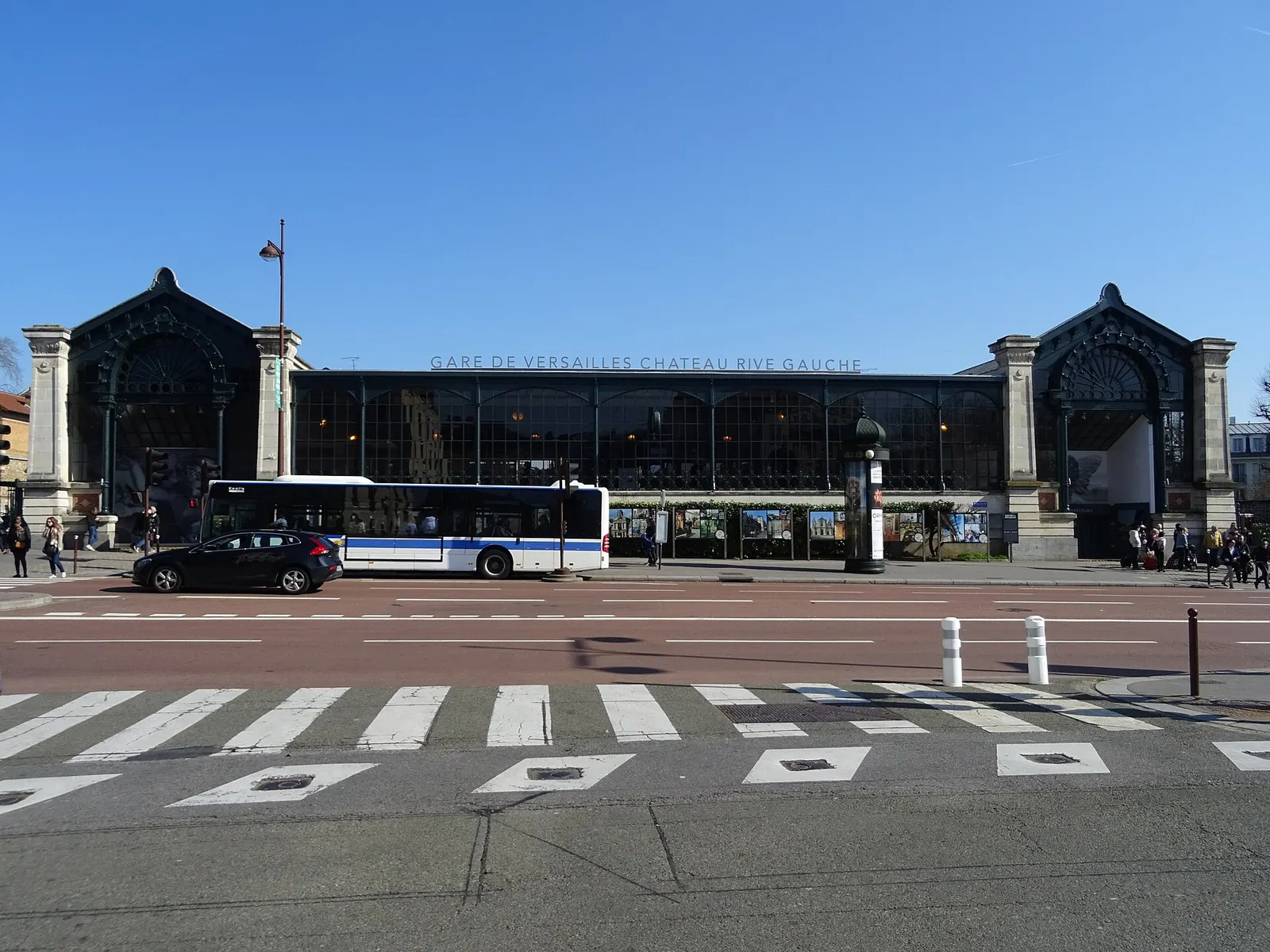 Glass and iron facade of Versailles Château Rive Gauche station with a bus passing in front, clear day